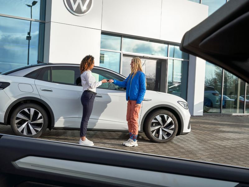 Eine VW Serviceangestellte überreicht einer Kundin den Schlüssel zu ihrem VW ID. 3