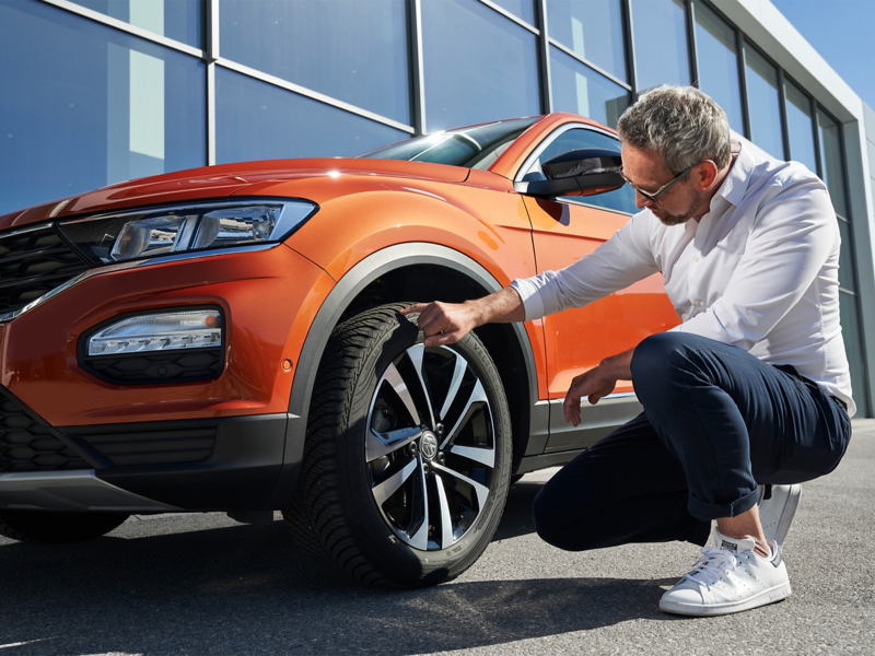 Man inspecting front tyre of VW car