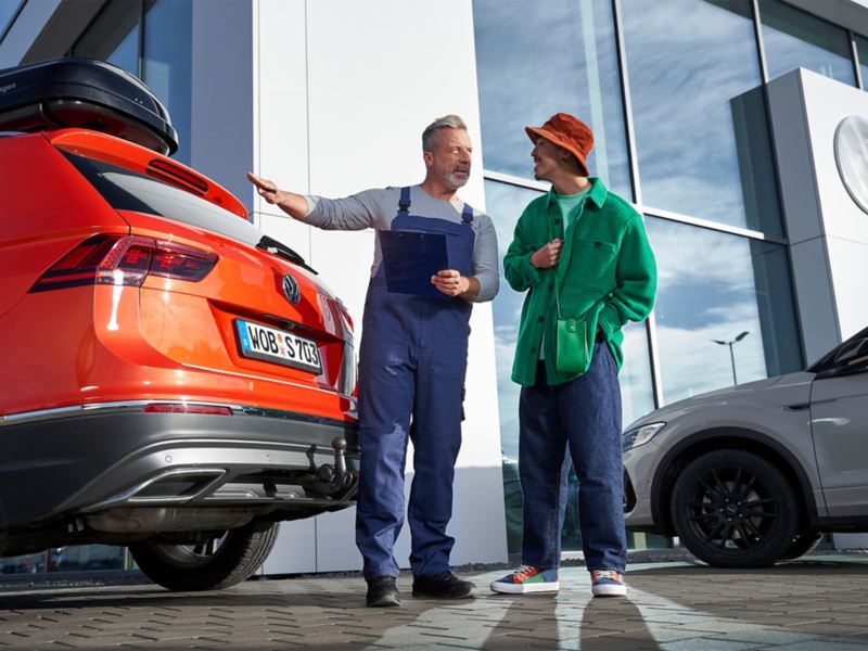 „Volkswagen“ darbuotojas rankoje laiko pagrindą rašymui su spaustuku ir kalbasi su klientu