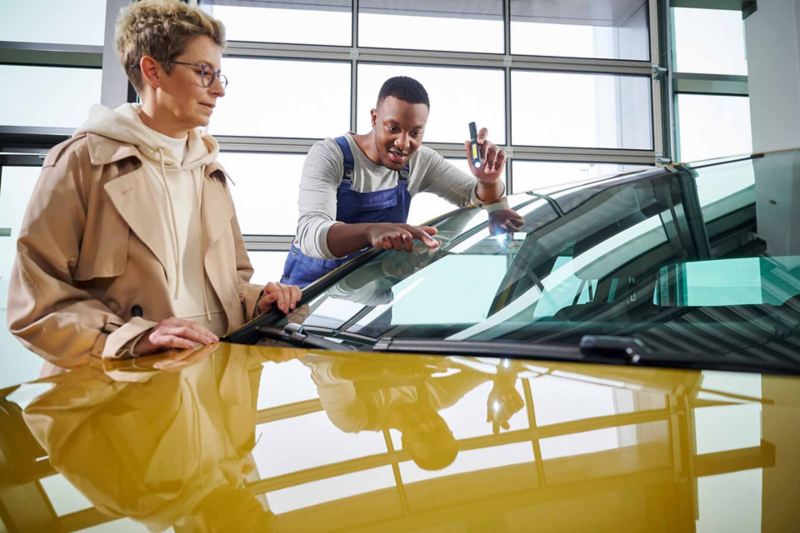 Un meccanico Volkswagen indica ad una cliente il parabrezza di un'auto.