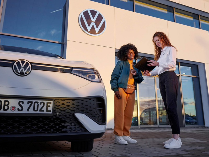 Une experte Volkswagen discute avec une cliente devant une concession.