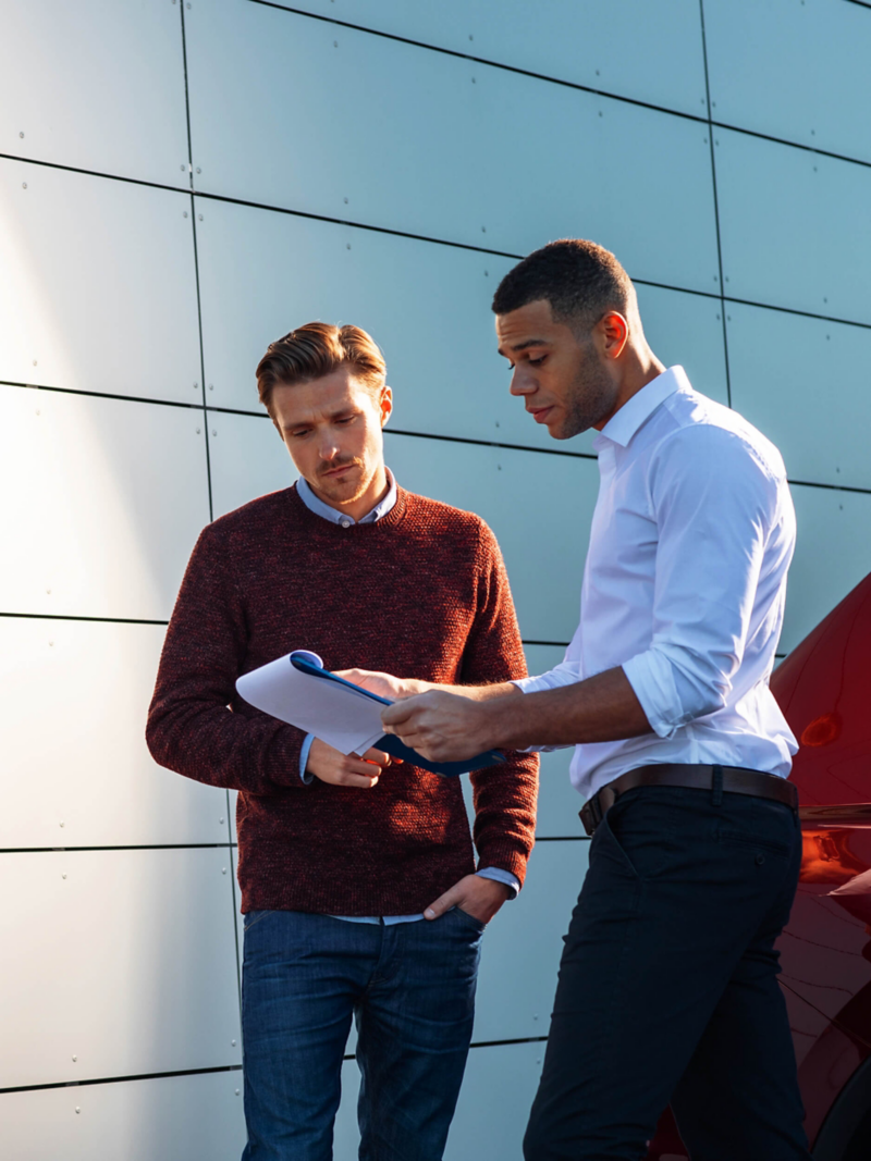 A VW retailer advisor and a customer outside of a building looking a a clipboard.