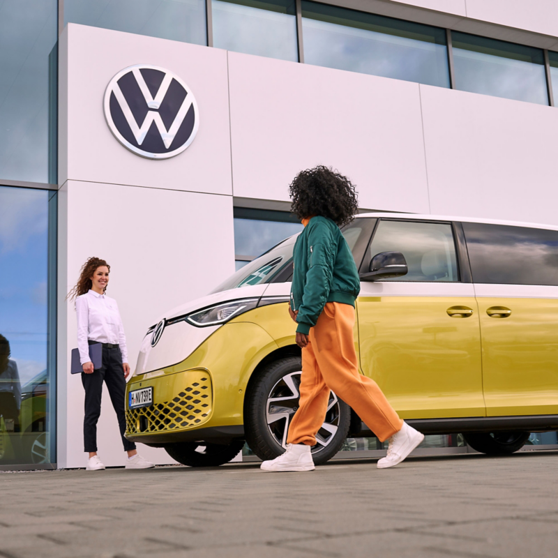 Una mujer del servicio técnico de VW hablando con una mujer, al lado del VW ID. Buzz.