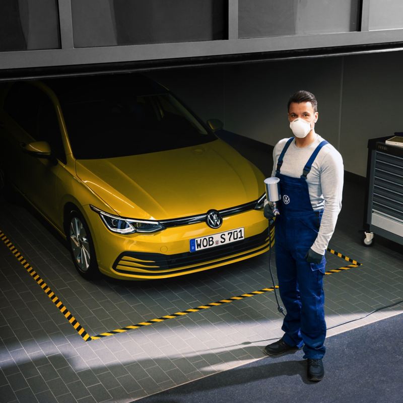 Skadespecialist står framför gul Volkswagen i ett garage