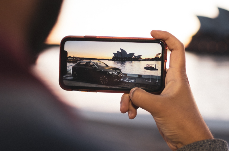 Image of a phone taking a picture of a car with Sydney Opera House in the background