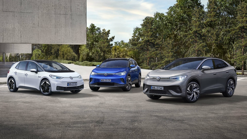 VW ID.3 in white, VW ID.4 in blue and VW ID.5 in grey on a car park in front of a building and trees