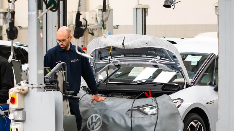 A technician working standing in front of a VW with the bonnet raised