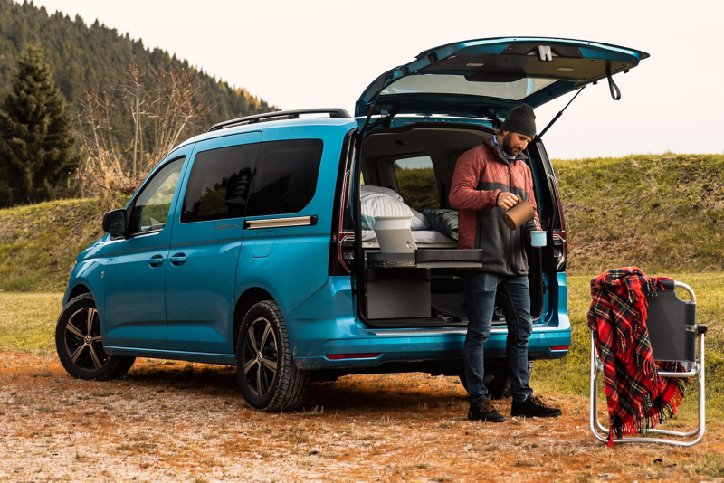 Ein VW Caddy California Parkt an einem Waldstück.