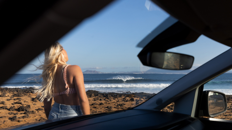 Surferin am Strand, fotografiert aus dem Innenraum eines VW Caddy California.