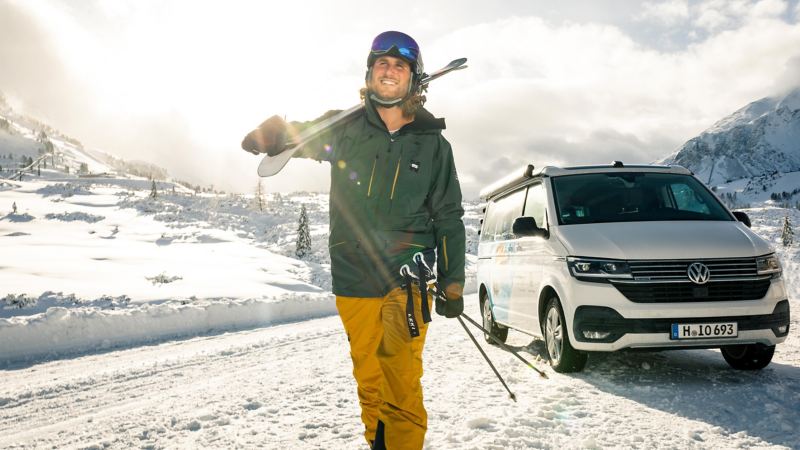 Snowboardåkare går bredvid en VW California i vinterlandskap