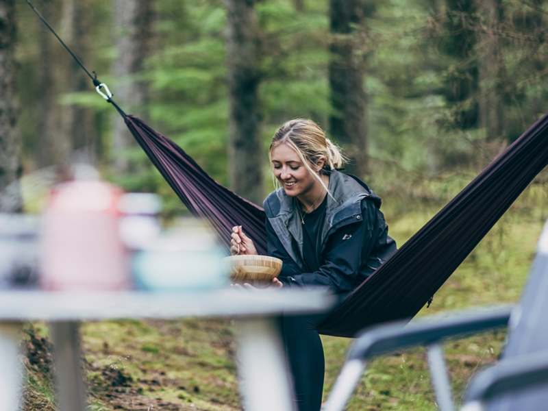 En kvinna sitter i en hängmatta och äter.