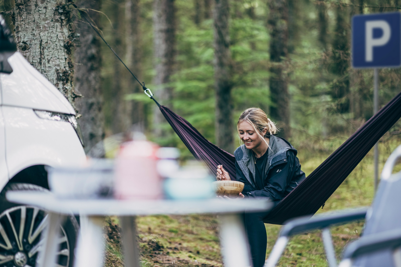 une femme mange un repas assise dans un hamac en forêt