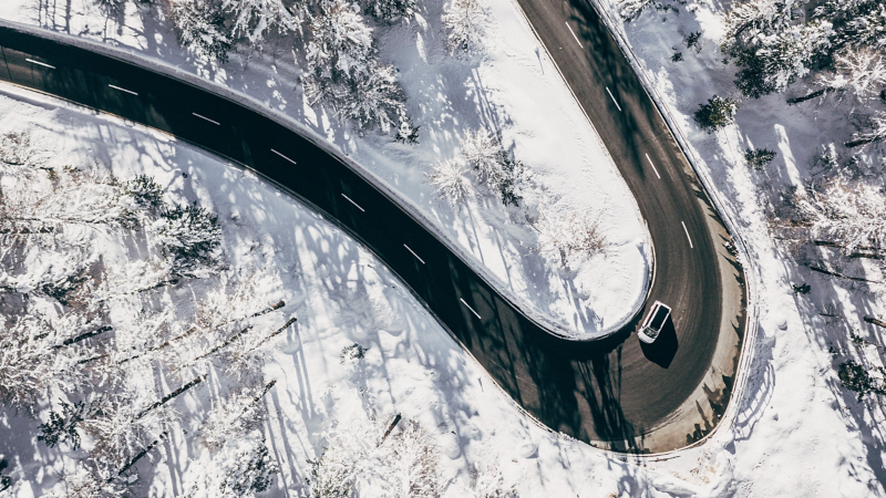 Ein Auto fährt auf einer Landstraße umgeben von einer Schneebedeckten Landschaft aus der Vogelperspektive.