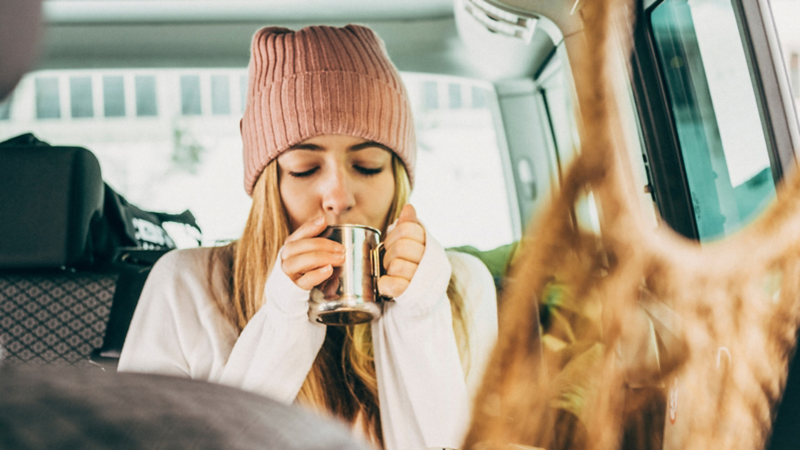 Eine junge Frau mit Mütze trinkt von ihrer Tasse.