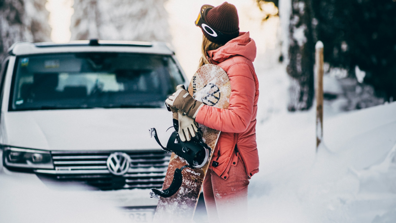 A snowboarder next to a VW California.