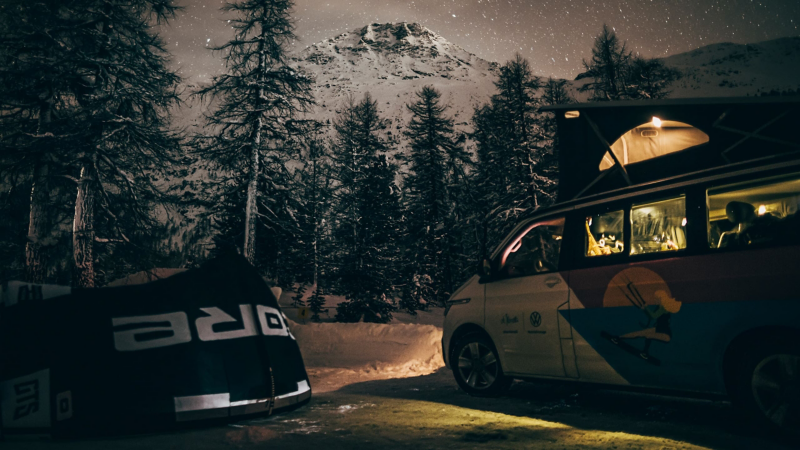VW California z podniesionym namiotem dachowym w zaśnieżonym lesie.
