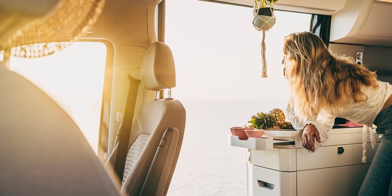 Une femme prend appui sur le bloc cuisine d’un Grand California dont la porte latérale est ouverte.