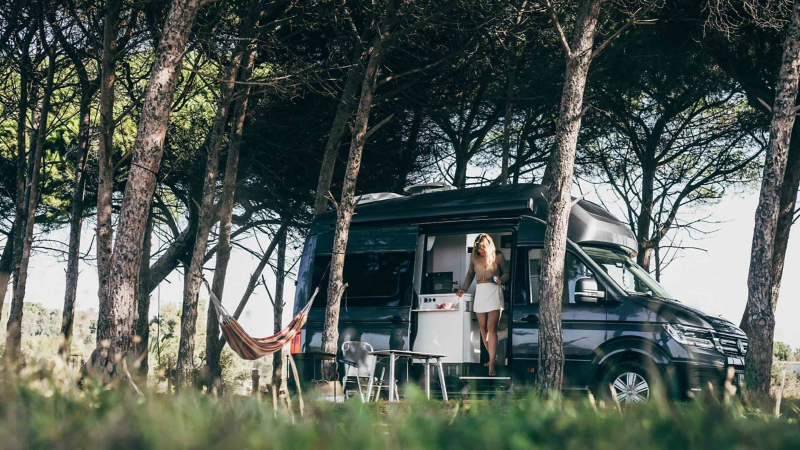 VW Grand California beneath some trees.