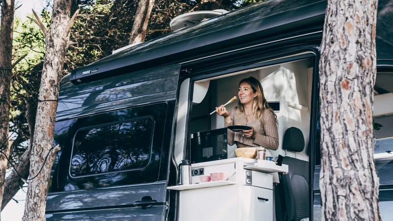 Eine Frau steht in der Küche eines VW Grand California und macht sich dort was zu essen.