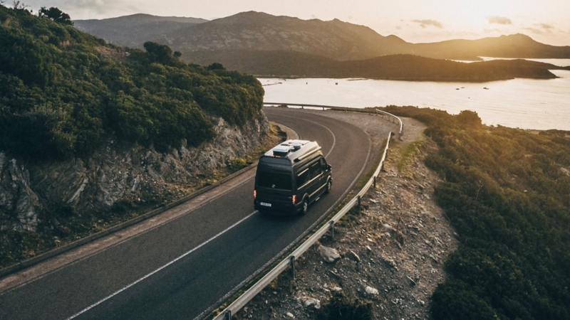Le van camping-car VW Grand California longe une route de bord de mer.