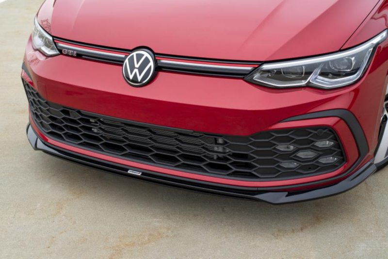 Gros plan sur la calandre et le pare-chocs avant d’une Volkswagen rouge avec design en nid d’abeille et becquet sport inférieur.