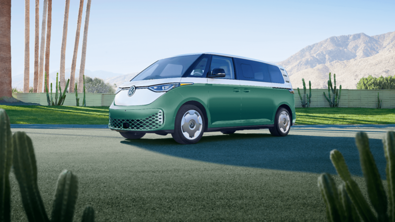 A green and white Volkswagen ID. Buzz 2025 parked on a scenic road with green hills in the background.