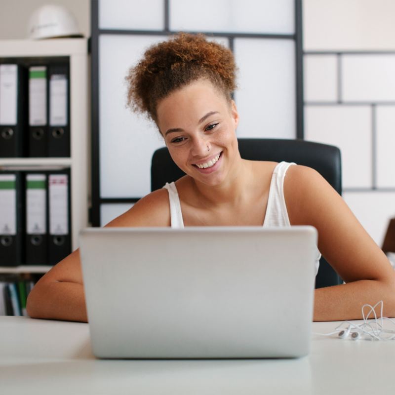 Lächelnde Frau sitzt an einem Schreibtisch und schaut auf ihren Laptop