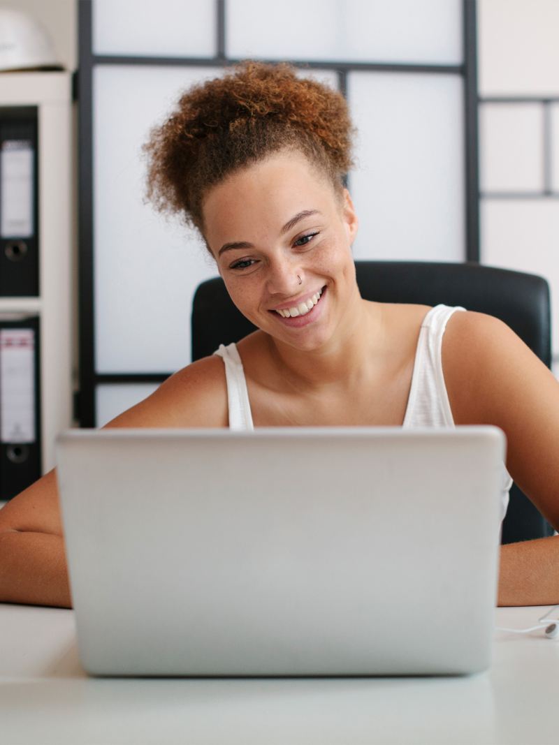 Lächelnde Frau sitzt an einem Schreibtisch und schaut auf ihren Laptop