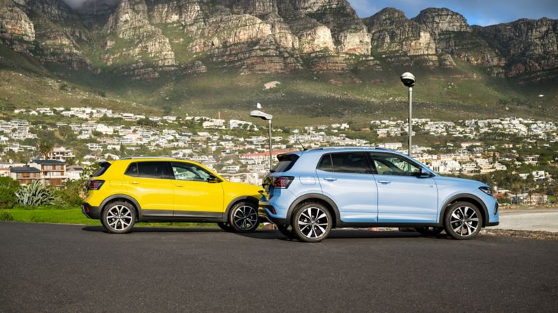 A yellow and a blue VW T-Cross drive past each other on a road in the city.