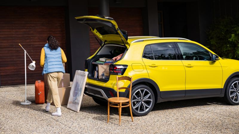 A young woman pushes a ladder through the open boot lid of a yellow VW T-Cross.