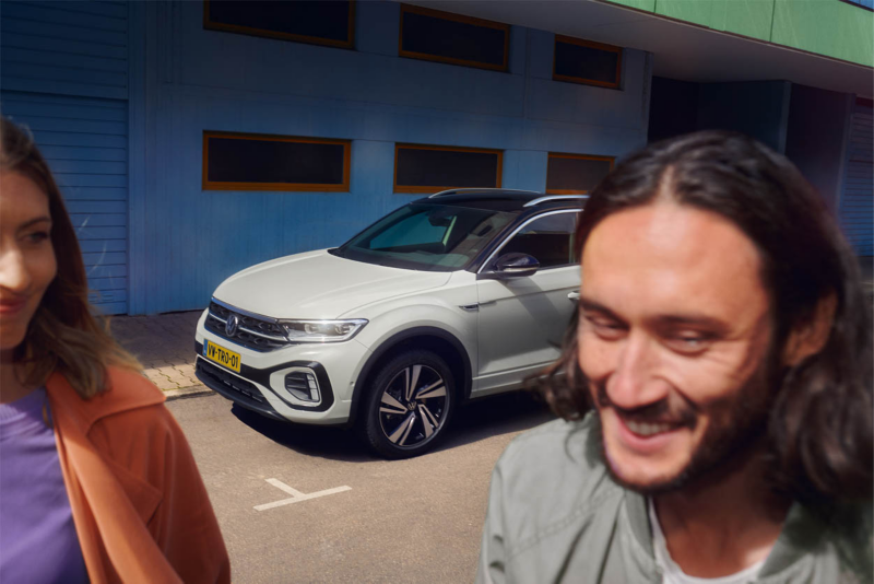 Vrouw loopt naast een witte Volkswagen T-Roc die geparkeerd staat naast een gebouw