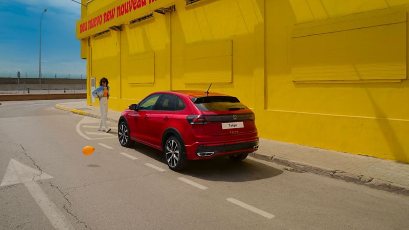 Una ragazza si allontana da una Volkswagen Taigo parcheggiata a bordo strada, vista lateralmente.