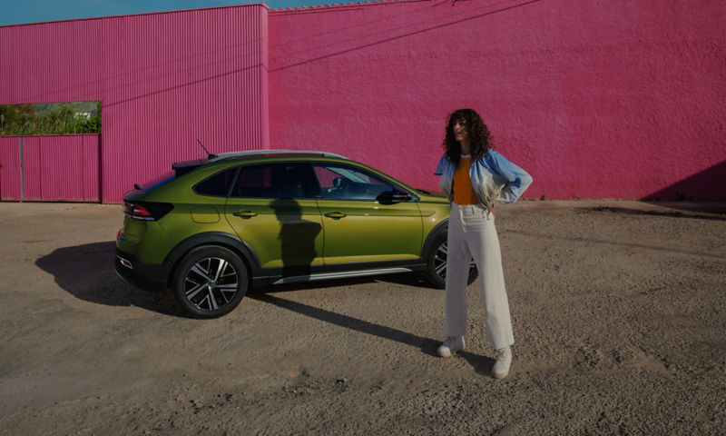 Une femme se tient debout devant un Taigo vert stationné sur un parking.