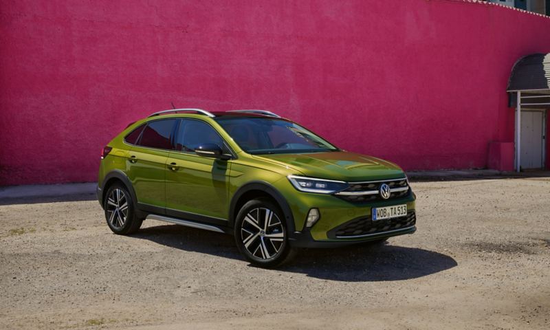 Groene VW Taigo Style voor- en zijaanzicht op parkeerplaats voor roze gebouw