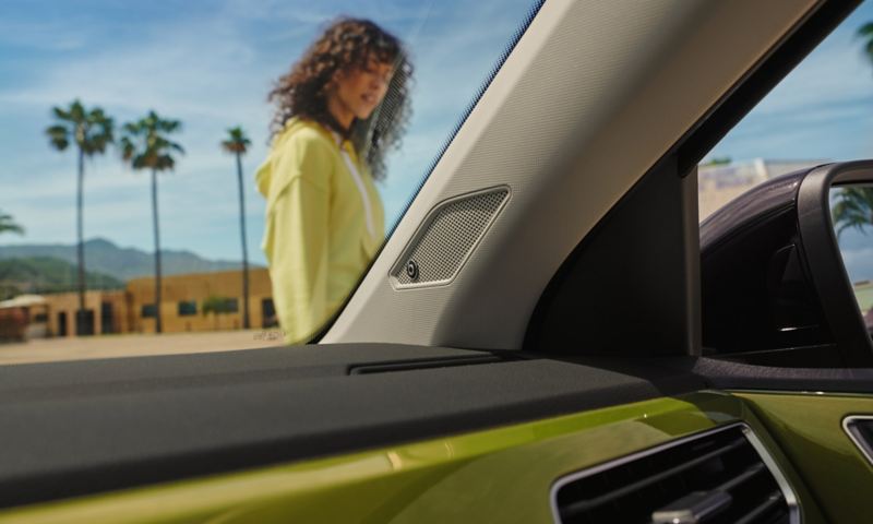 Blick durch die Windschutzscheibe des VW Taigo auf eine Frau, Lautsprecher des optionalen BeatsAudio™ Soundsystem im Zentrum