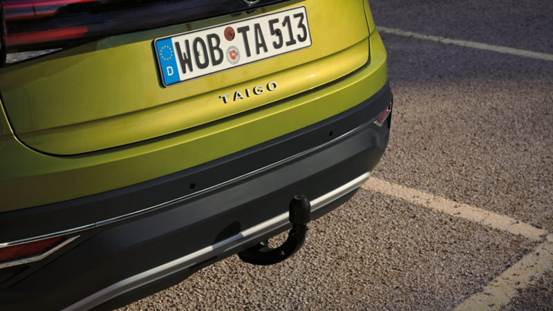 Detailansicht der optionalen Anhängerkupplung am Heck eines grünen VW Taigo.