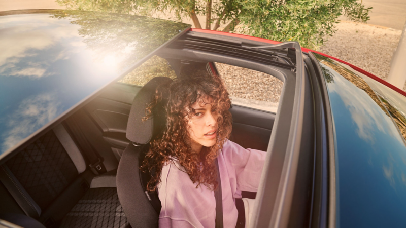 VW Taigo: Blick durchs optionale Panorama-Ausstell/-Schiebedach auf Frau im Fahrersitz.