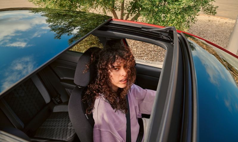 VW Taigo: View through optional tilting and sliding panoramic sunroof to a woman sitting in the driver seat
