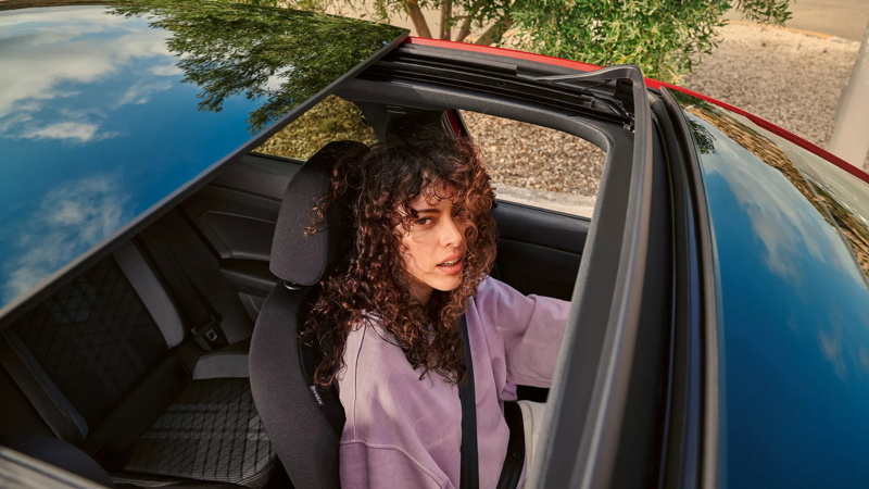 Vrouw zit achter het stuur van Volkswagen Taigo, ze kijkt door het geopende panoramische glazen schuif/kanteldak