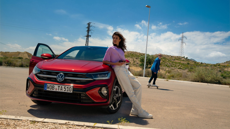 VW Taigo R-Line in Rot, Frontansicht auf Parkplatz. Frau lehnt an Motorhaube, Mann fährt Skateboard