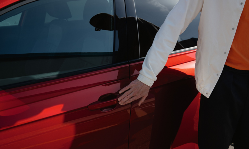 A man touches the door handle of a red VW Taigo with his hand