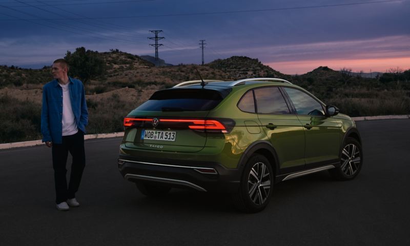Volkswagen Nouveau Taigo vert avec un homme debout devant dans la pénombre