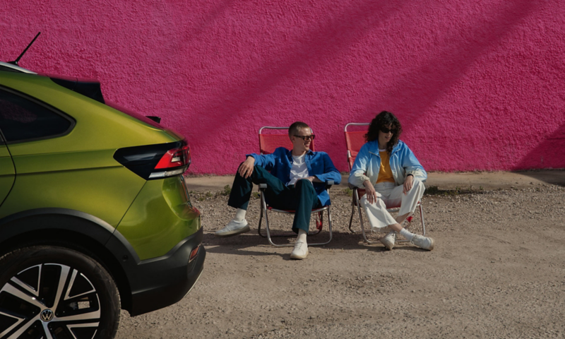 Rear of green VW Taigo, two people are sitting on camping chairs behind it