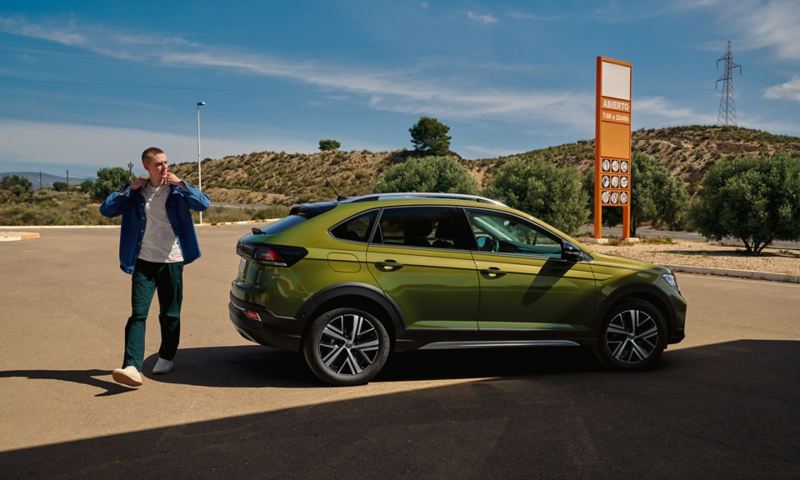 Volkswagen Taigo di colore verde in posizione di parcheggio, vista laterale, un uomo passa a fianco dell’auto