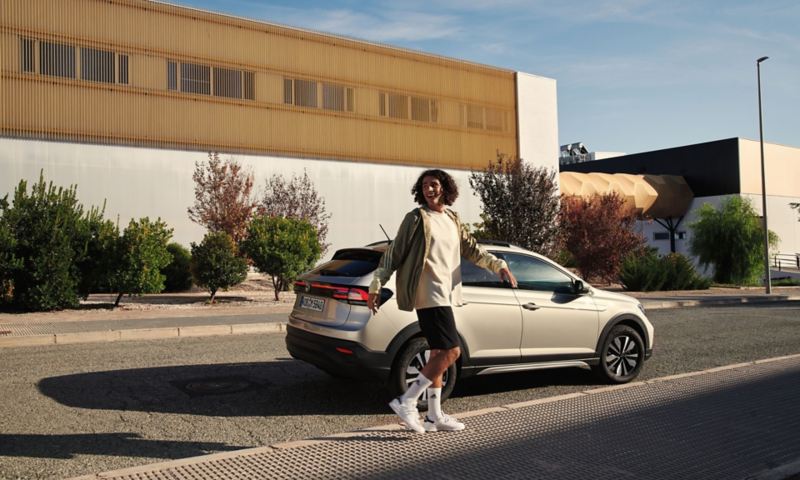 VW Taigo MOVE in silber parkt am Straßenrand, Blick auf die Rückleuchten, ein junger Mann läuft daran vorbei