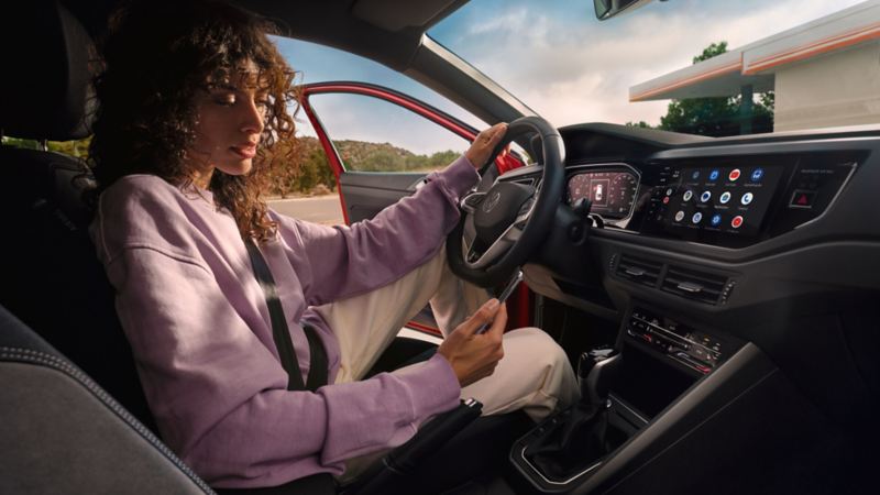 VW Taigo interior: Woman sitting in the driver seat in a parked car looking at her smartphone