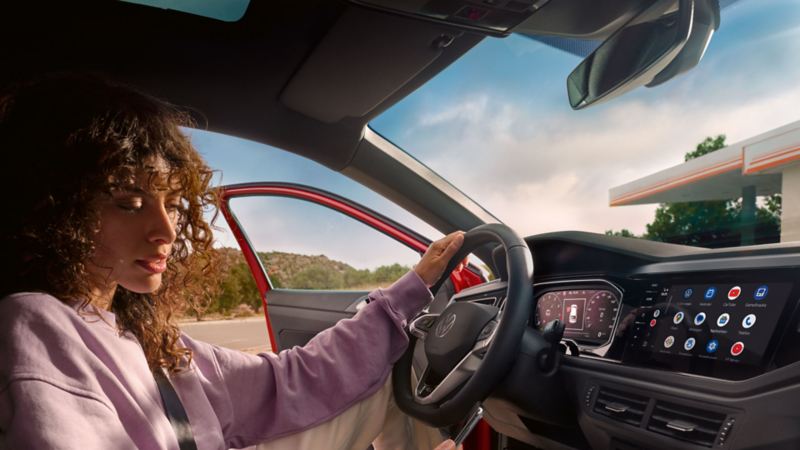 VW Taigo Interieur: Frau sitzt auf Fahrersitz in parkendem Auto und schaut aufs Smartphone