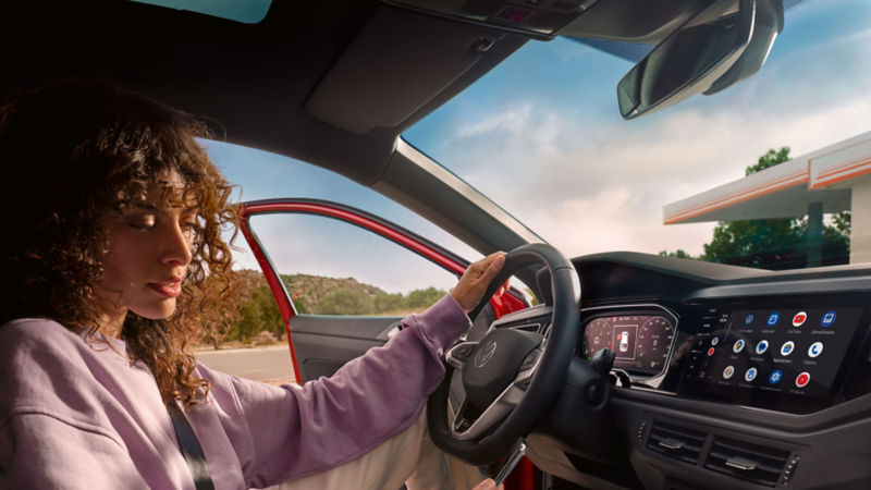 VW Taigo interior: Woman sitting in the driver seat in a parked car looking at her smartphone