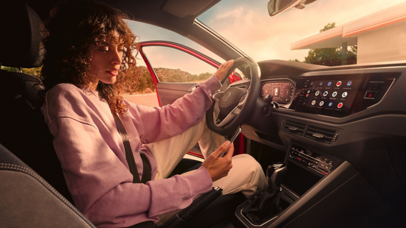 VW Taigo Interieur: Frau sitzt auf Fahrersitz in parkendem Auto und schaut aufs Smartphone.