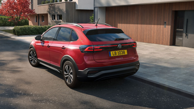 Une VW Taigo rouge est garée au bord de la route devant le garage d'une maison individuelle moderne.